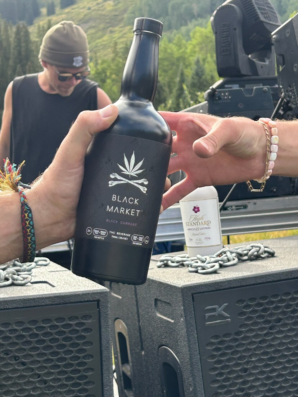 A DJ in a green hat behind a hand-held Black Market bottle at an outdoor Garden Session.