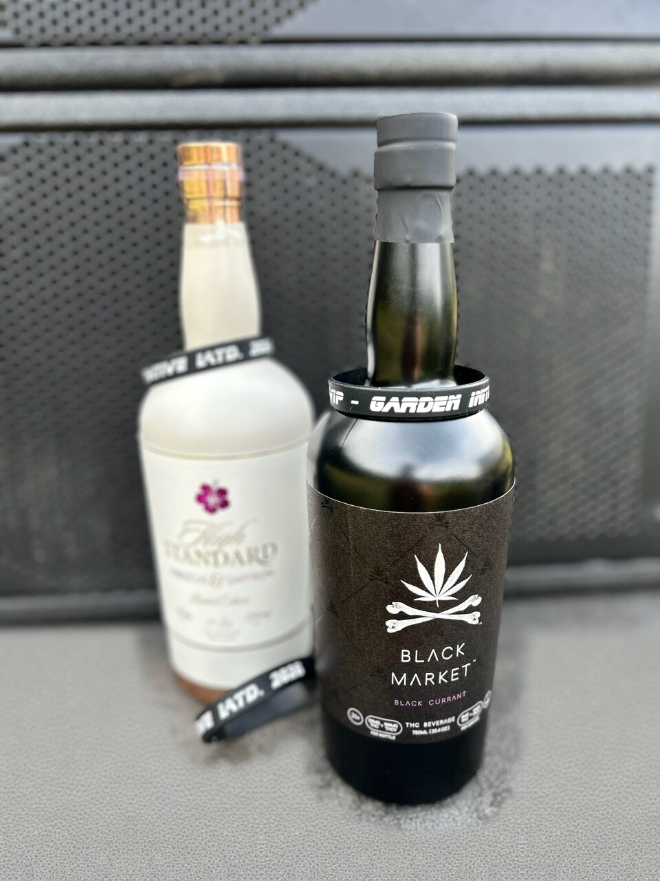 Black Market and High Standard bottles with Garden Initiative wristbands beside sound equipment.